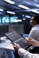 Computer scientist in server hub using tablet to find firewall misconfigurations affecting performance. IT staff member checking systems bottlenecks leading to sluggish data transfer rates, close up photo