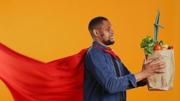 African american guy posing as a superhero with fresh ripe produce, hero with red cape promoting ethically sourced food and zero waste. Male model supports local farming. Camera B. photo