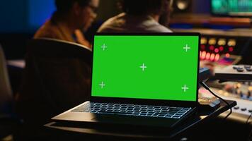 Sound designer and singer look at laptop with isolated display in control room, operating mixing console and volume level buttons to create a hit song. Artist working with audio expert. Camera A. photo