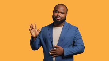 African american man reluctantly doing salutation hand gesture, saying goodbye. Portrait of sad BIPOC person raising arm to greet someone after leaving, isolated over studio background, camera A photo