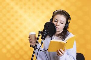 Woman doing voiceover, reading of ebook on ereader to produce audiobook, holding coffee cup. Narrator using storytelling skills while reading text from tablet, recording novel, enjoying caffeine drink photo