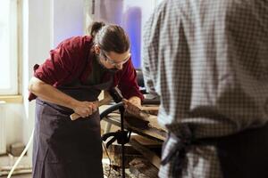 Experienced woodworker shaping raw timber using chisel and hammer in carpentry shop, enjoying diy hobby. Woodworking professional in studio shaping wooden pieces with tools, making wood sculptures photo