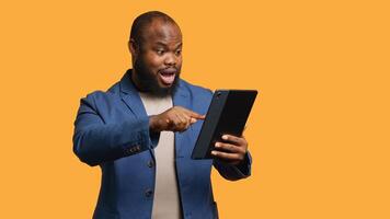Man happily scrolling on tablet touchscreen to check social media feed. African american person browsing internet websites, entertained by content, studio background, camera A photo