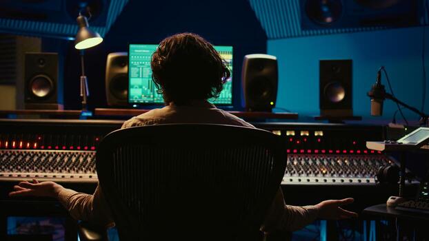Music engineer producing sounds with mixing console and daw software interface, working on a new album. Technician uses audio console with moving faders and colored meters. Camera B. photo
