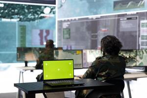 Laptop running isolated green screen display in command center military base, working on surveillance for new defense missions. Troopers working on reconnaissance in control room. photo