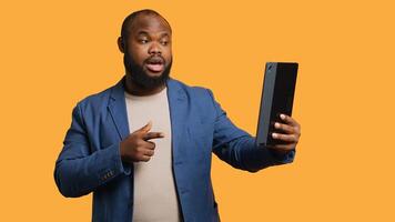Joyful man having entertaining conversation with friends during teleconference meeting using tablet, studio background. Happy person having fun interacting with mates during online videocall, camera A photo