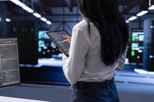 Engineer doing yearly checkup to prolong data center electronics life span and avoid downtime. Woman in server room monitoring server infrastructure components using tablet photo