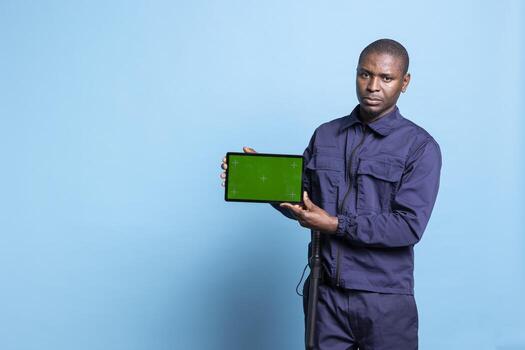 Security officer using a tablet to show an isolated copyspace screen on camera, wearing his work uniform and smiling. Proud bodyguard presenting mockup display on device in studio. photo