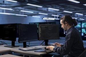 Admin working on computer to check for signs of imminent failure in data center infrastructure. IT expert working at PC desk to prevent damages in server hub, monitoring critical systems photo