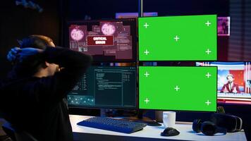 Scammer hacking using green screen PC and getting critical error notification while trying to infiltrate banking systems. Hacker runs script on chroma key display, failing to breach firewall, camera B photo