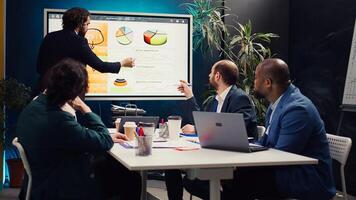 Project manager does a market research presentation for his team, better understanding of the situation. Associates work on technology or infrastructure investments to fulfill objectives. Camera B. photo
