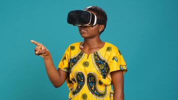 Gorgeous girl in ethnic clothes using vr glasses against blue background, working with high tech 3d experience with virtual reality device. Young woman using smart headset. Camera A. photo