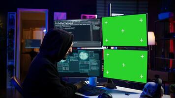 Hacker developing spyware software on green screen computer to steal important data to be sold on black market. Hooded scammer writing malicious code on chroma key PC, camera B photo