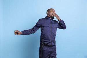 African american security guard feeling exhausted in front of camera, working on safeguarding a property. Male bodyguard yawning and showing signs of burnout after a night shift. photo