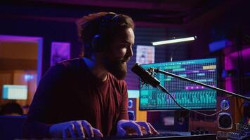 Musician playing piano midi controller and recording a new song, singing on microphone in his home studio. Sound engineer working on digital audio workstation, using electronic keyboard. Camera B. photo