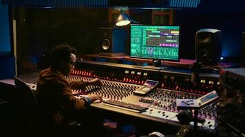Portrait of professional sound engineer recording tracks and editing tunes by adjusting volume levels with knobs. Producer creating music with mixing console in post production studio. Camera B. photo