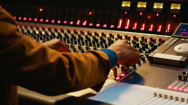 Audio technician producing new music at mixing console in control room, twisting knobs, pressing sliders and switchers. Producer working on processing and editing sounds quality. Camera A. photo