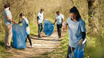 Environmental activist picking up trash with a claw tool and recycling, protecting the natural forest habitat and doing litter cleanup. Woman doing voluntary work to stop pollution. Camera A. photo