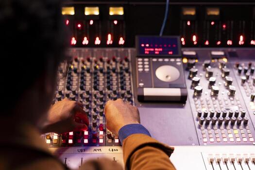 African american audio technician pushing sliders and switchers on panel board in control room, processing music for a new album. Producer working with mixing console and editing software. photo