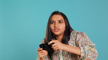 Gamer annoyed after losing online multiplayer videogame, being defeated by rival players. Indian woman upset after seeing game over message, holding controller, studio background, camera B photo
