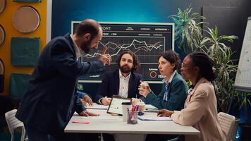 Business analysts meeting in a boardroom to discuss project stages and updates, gathering information from data reports and planning steps to coordinate with objectives. Employee engagement. Camera B. photo