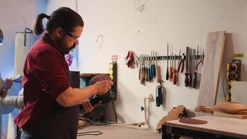 Carpenter holding power tool used to smooth surfaces by abrasion with sandpaper, changing cut off discs. Man preparing necessary equipment for furniture assembling job in studio, camera B photo