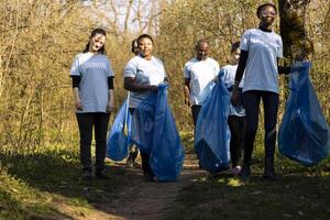 Team of volunteers doing community service to collect garbage and help preserve natural ecosystem, gathering to clean the forest. Diverse group fighting pollution and illegal dumping. photo