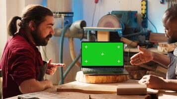 Upbeat men using CAD software on isolated screen laptop, debating wood design to use. Smiling cabinetmakers chatting, using program on chroma key notebook to make furniture schematics, camera A photo