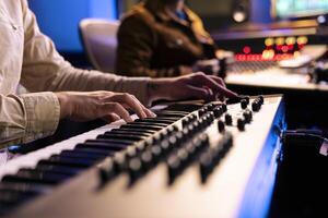 Young composer songwriter recording his piano notes in control room, playing electronic keyboard in professional studio. Talented musician performing live on midi controller synthesizer. Close up. photo