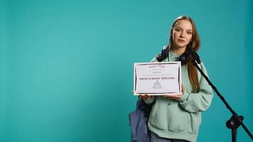 Overjoyed student celebrating achievement, holding diploma, using microphone to do speech, studio background. Woman using mic to share wisdom with colleagues after finishing school, camera B photo