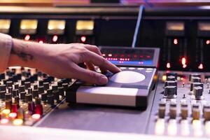 Skilled sound engineer operating mixing console and motorized faders in studio, using technical equipment to edit and process new tracks in control room. Young composer producing songs. Close up. photo