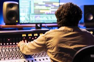 Audio engineer processing and composing tracks in control room, operating on digital software interface. Young sound technician mixing and mastering songs in professional studio, mixer station. photo