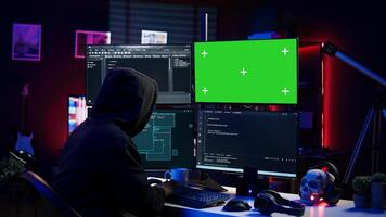 Hacker coding on isolated screen computer monitors, developing zero day exploit undetectable by antivirus. Evil IT engineer using chroma key PC displays to build script tricking firewalls, camera B photo