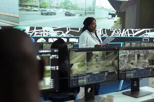 African american supervisor offers shipment information for delivery parcels to her team, employees monitoring traffic on routes. Order tracking in control center, satellite maps with gps. photo