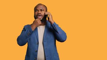 African american man having thoughtful conversation with friend during telephone call, studio background. Pensive BIPOC person talking on phone with mate, doing thinking gesturing, camera A photo