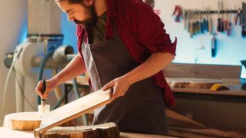 Cabinetmaker applying varnish on wooden surface to prevent damage and provide layer of protection. Woodworking expert in studio doing finishing on wood plank, putting coats of oil, camera A photo