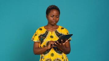 Natural cute girl browsing internet on a tablet against blue background, navigating on online web pages by using a portable device. Woman posing with a gadget and traditional outfit. Camera A. photo
