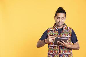 Indian man adding payment method on website using tablet, purchasing stuff, isolated over studio background. Client does internet shopping, typing debit card info on device photo