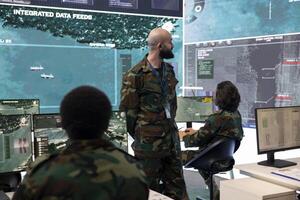Trooper in camouflage uniform supervising surveillance systems in control room, ensuring operational success. Recruits team analyzing real time radar to support federal agency missions. photo