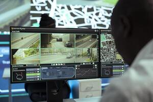 African american operator monitoring traffic on streets and locating couriers, tracking parcels to update clients on order shipment. Male employee operates on CCTV footage, gps tracing. photo