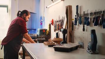 Carpenter selecting tool from rack to use on wood materials, helped by african american coworker. Craftsperson doing quality assurance on lumber pieces pile with BIPOC apprentice, camera B photo