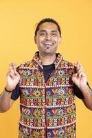 Portrait of joyful hopeful man crossing fingers, wishing to receive good news, studio backdrop. Upbeat person with positive facial expression hoping for good luck, aspiring for miracle photo