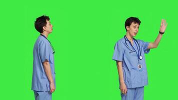 Woman nurse waving hello and inviting people to come closer, calling over patients for checkup examinations against greenscreen. Medical assistant greeting persons and asking them to come. Camera B. photo