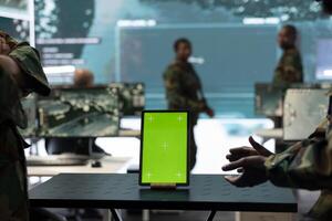 Two servicemen working together with an isolated copy space screen, using a tablet to help troopers in power base command post. Soldiers team examine real time information on device. Close up. photo