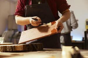 Cabinetmaker applying varnish on wooden surface to prevent damage and provide layer of protection, close up shot. Woodworking professional in studio doing finishing on wood plank, putting coats of oil photo