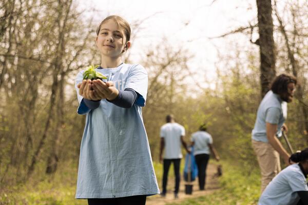 Little kid volunteer showing small seedling with natural soil in her hands, new habitat in the forest. Small girl fighting for nature preservation, cultivating consciousness and with activists.