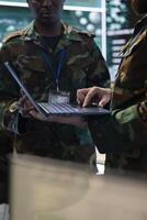 Diverse military personnel analyzing real time data on a laptop, transmitting important mission information for the infantry unit. Special operations soldiers working in command post. Close up. photo