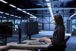 Programmer coding on PC, doing maintenance in data center to extend equipment life span and avoid downtime. Indian woman monitoring blade servers for overheating problems photo