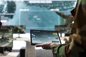 Army conscript detecting targets on a satellite world map to ensure national safety, operates on tablet in military power base of operations. Private examines battlefield real time data. Close up. photo