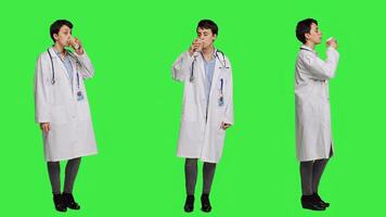Happy medic serving hot coffee cup as refreshment against greenscreen backdrop, wearing white coat and drinking caffeine beverage. General practitioner enjoying drink, medical expertise. Camera A. photo